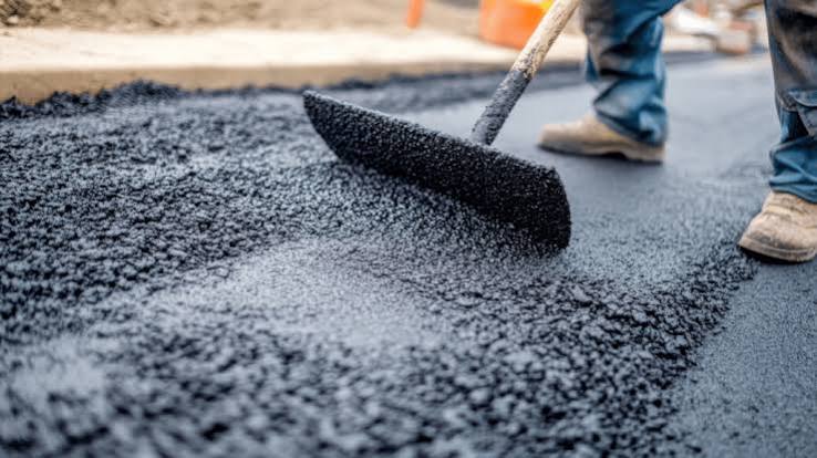 A crew raking fresh hot asphalt into place during a driveway repair