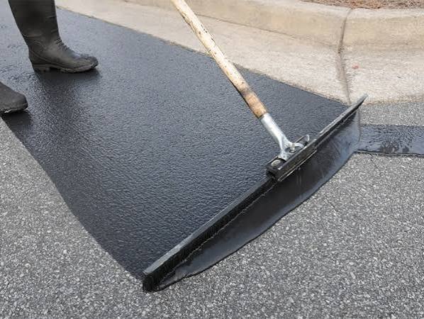 A squeegee spreading fresh sealcoat across an asphalt driveway