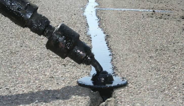 Hot rubberized sealant being applied into an asphalt driveway crack