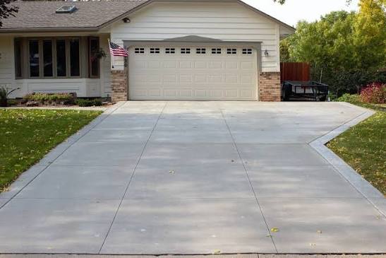 A clean, freshly resurfaced concrete driveway in front of a home
