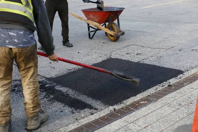 A crew patching a freshly cut pothole with new asphalt next to a wheelbarrow